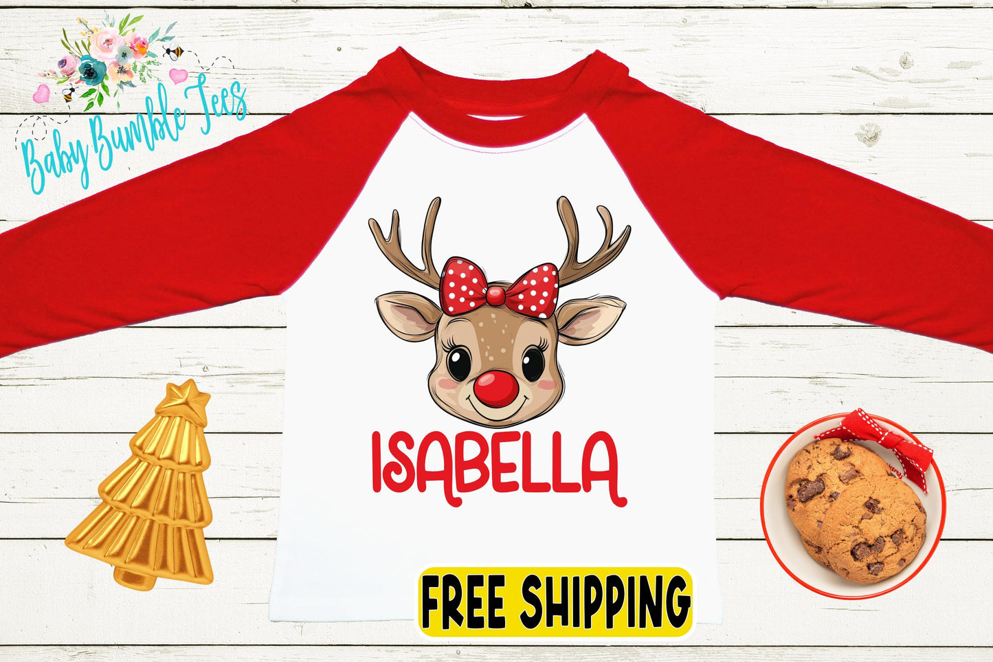 a red and white long-sleeved shirt with a cartoon reindeer wearing a red bow and the name "Isabella" printed on it. The shirt is displayed on a white wooden background, along with a small Christmas tree, a cookie, and a sign that says "FREE SHIPPING".