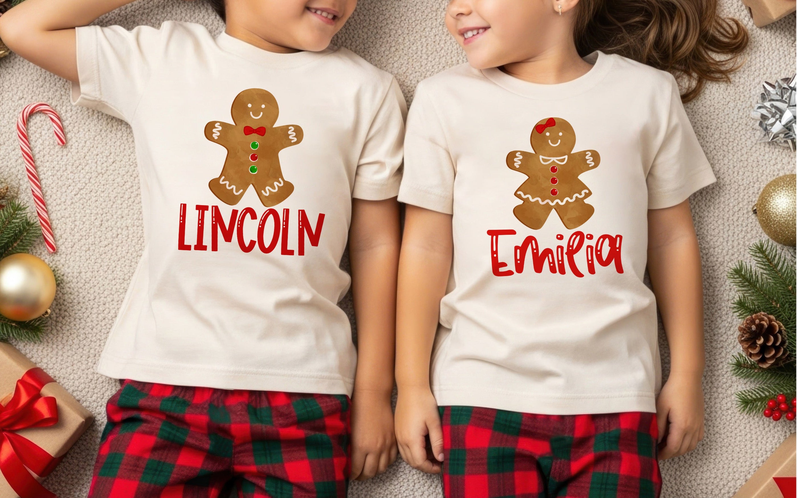 Two children wearing white t-shirts with gingerbread men graphics and names, surrounded by Christmas decorations.