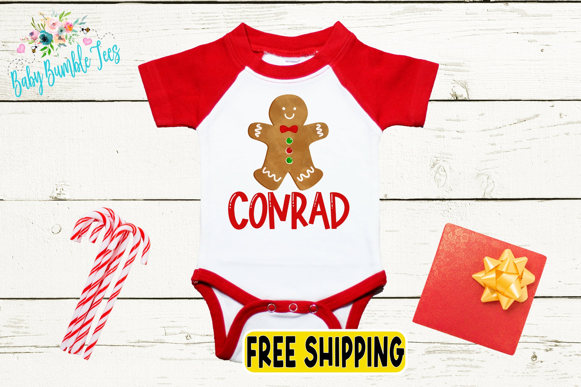 A red and white baby onesie with a gingerbread man design, a red bow, and a red ribbon, along with some candy canes and a red gift box, all placed on a white wooden background.
