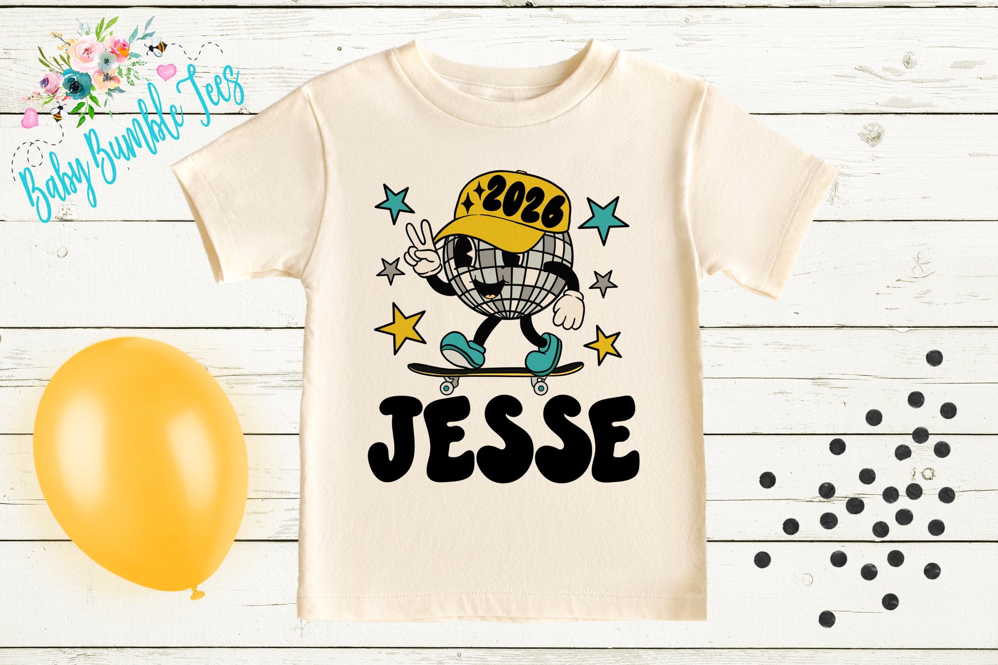 A white t-shirt with a cartoon character and text, along with a yellow balloon and scattered black dots on a white wooden background.