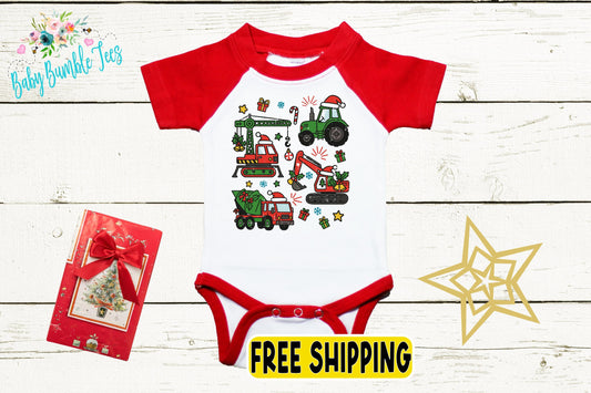 a red and white baby onesie with a Christmas-themed design, including a tractor, a fire truck, and other festive elements. The onesie is displayed on a white wooden background, along with a red gift box and a gold star decoration.