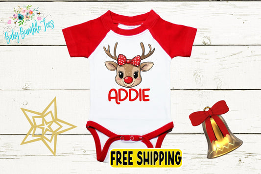 A red and white baby onesie with a cartoon reindeer and the name "Addie" printed on it, along with a bell and a star decoration.