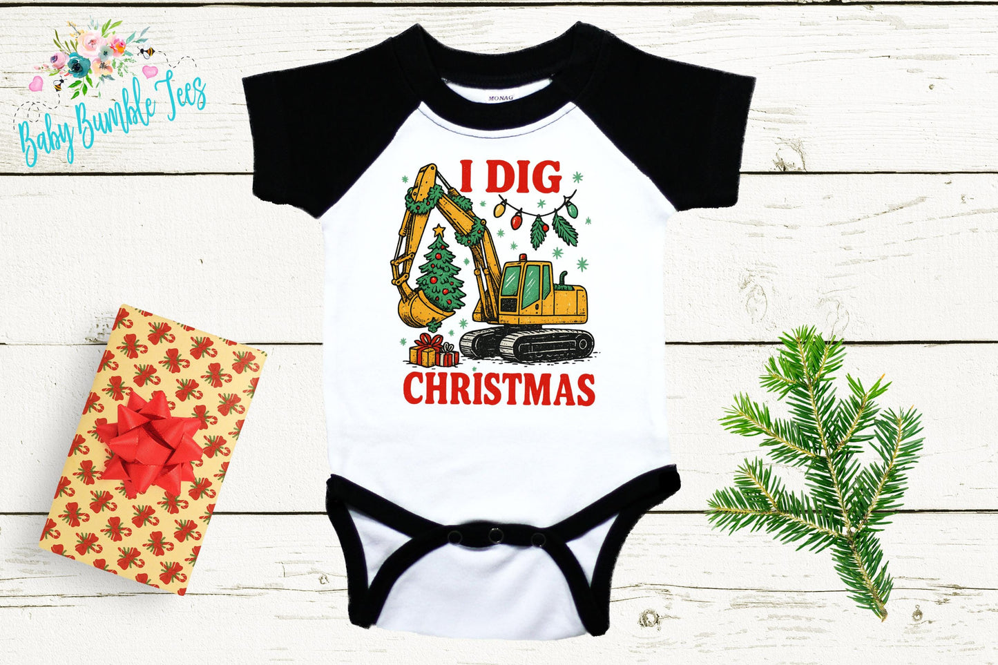A black and white baby onesie with a graphic of a construction vehicle and Christmas decorations, along with a gift box and a pine branch.