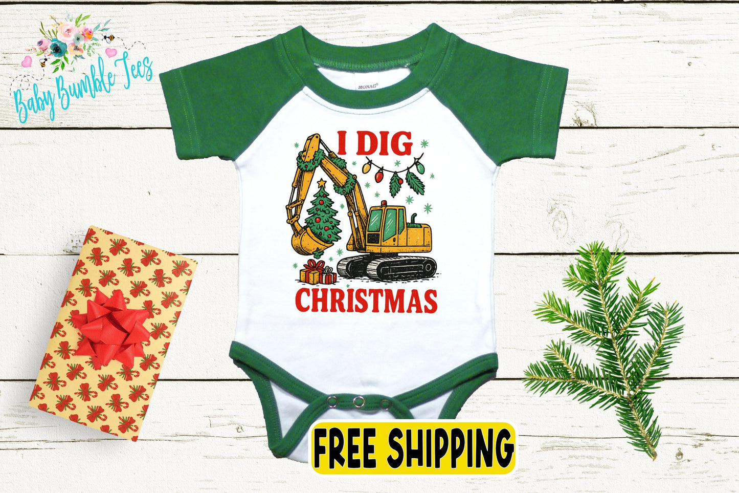 a baby onesie with a Christmas-themed graphic, including a yellow excavator digging a tree, a gift box with a red bow, and a pine tree branch.