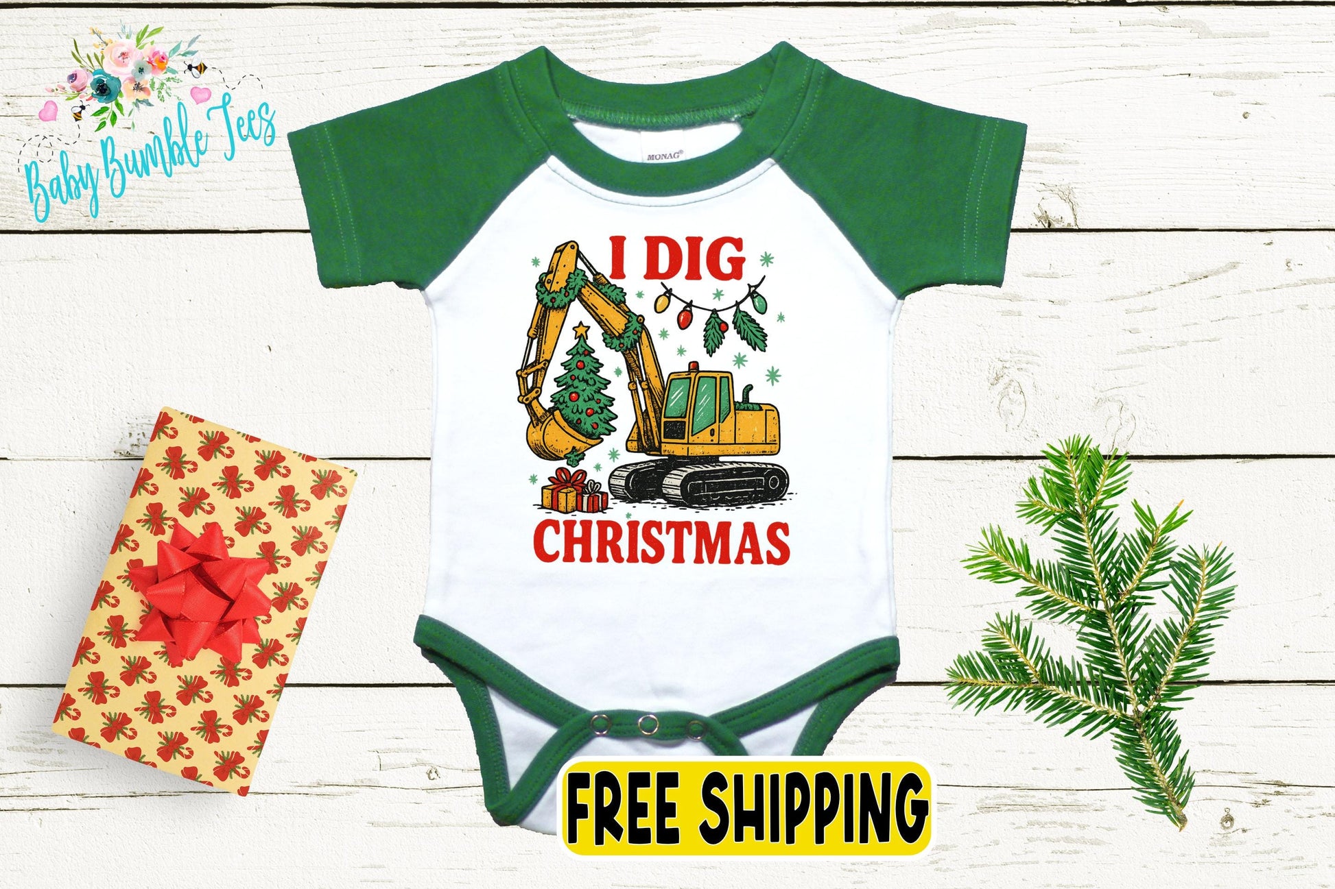 a baby onesie with a Christmas-themed graphic, including a yellow excavator digging a tree, a gift box with a red bow, and a pine tree branch.