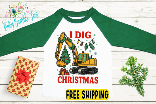 a green and white long-sleeved shirt with a graphic design depicting a yellow excavator digging up a Christmas tree, surrounded by Christmas decorations. The shirt also has the text "I Dig Christmas" and "FREE SHIPPING" printed on it.