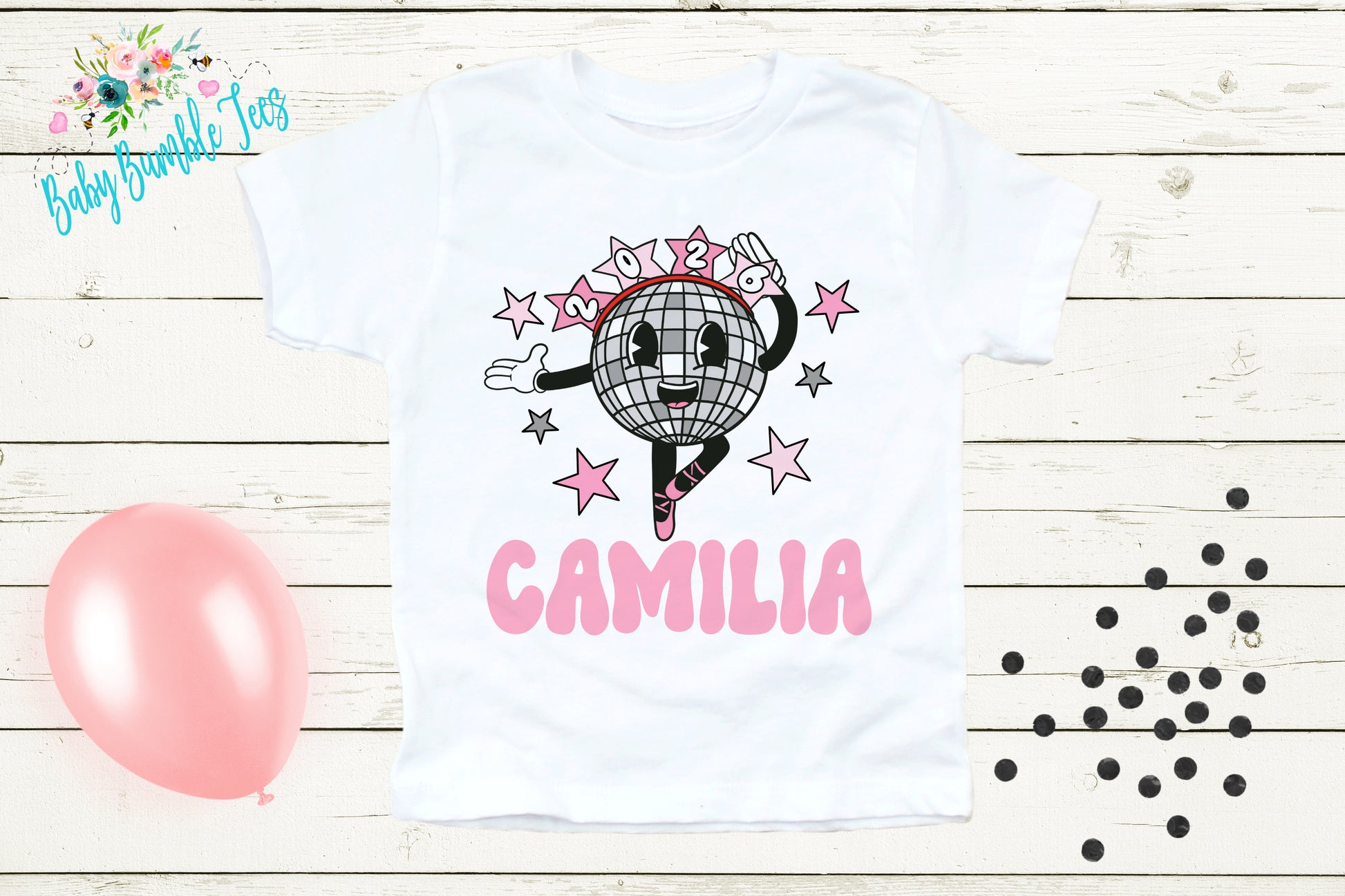 A white t-shirt with a cartoon image of a dancing disco ball and the name "Camilia" printed on it, along with pink stars and a pink balloon.