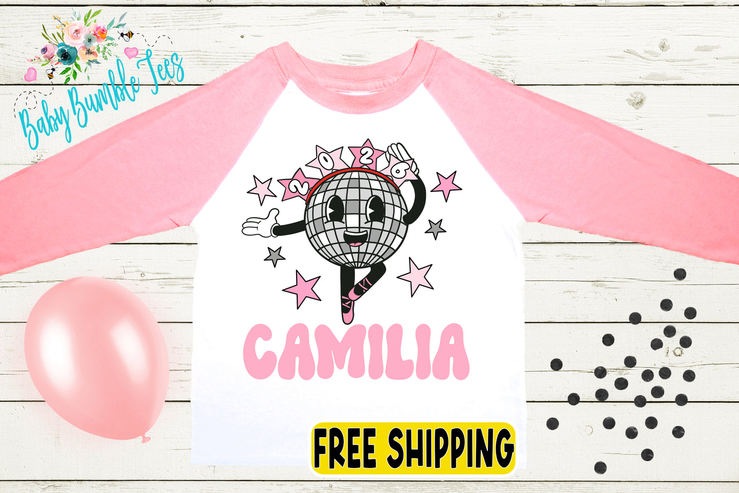 a pink and white long-sleeved shirt with a cartoon image of a disco ball and stars, along with the name "Camila" printed on it. The shirt is displayed on a wooden surface, and there are pink balloons and black dots around it.