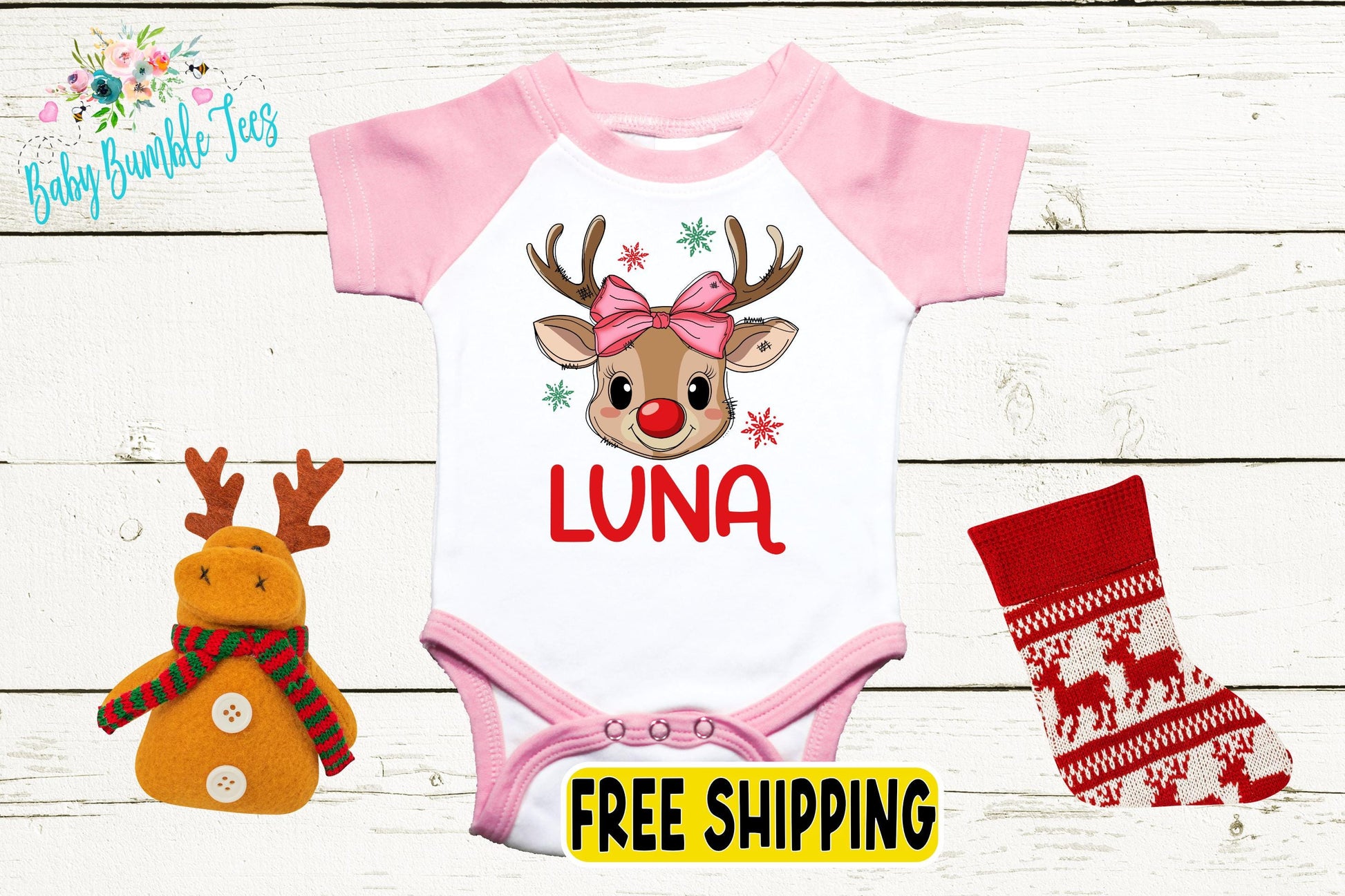 a pink and white baby onesie with a deer head design, a stuffed reindeer, and a red stocking.